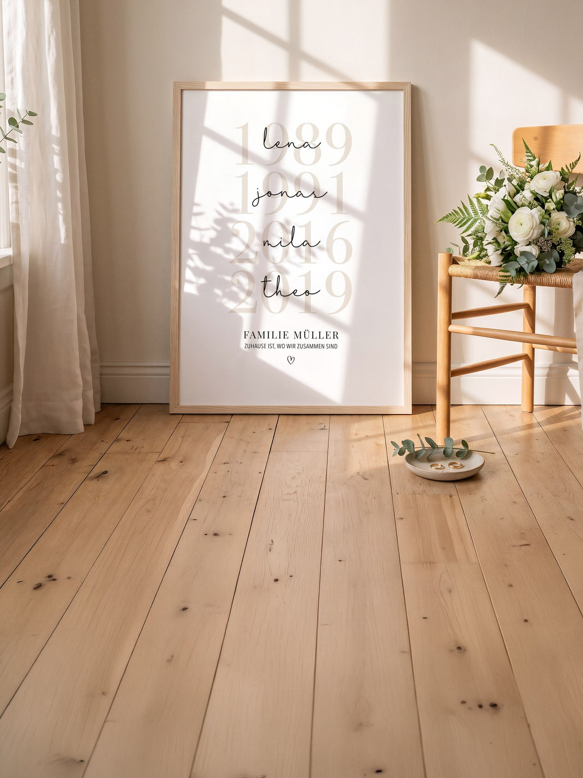 Großes Familienposter mit vier Jahreszahlen und Vornamen im hellen Holzrahmen an die Wand gelehnt, daneben ein Holzstuhl mit Blumen