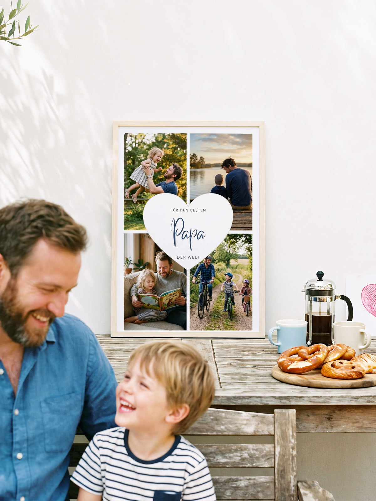 Fotocollage Herz Papa im Holzrahmen auf dem Terrassentisch, davor Papa mit seinem Sohn auf dem Schoß