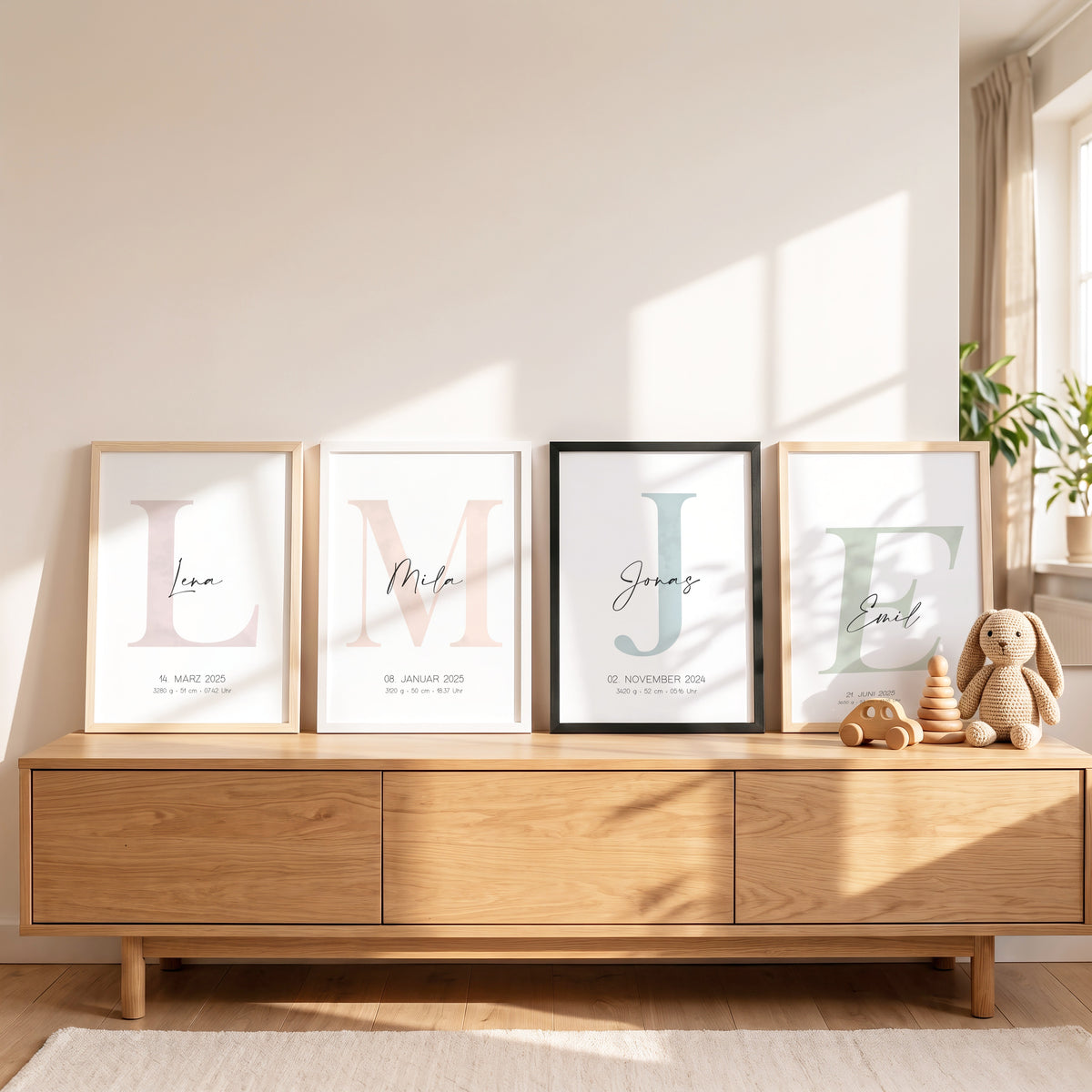 Vier Geburtsposter nebeneinander auf einem Sideboard: L in Altrosa, M in Apricot, J in Pastellblau und E in Pastellgrün