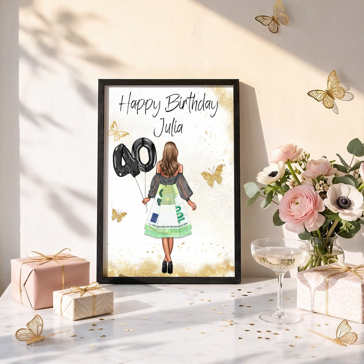 Poster mit Geldrock im schwarzen Rahmen auf einem Geschenketisch mit Blumen und Sektglas