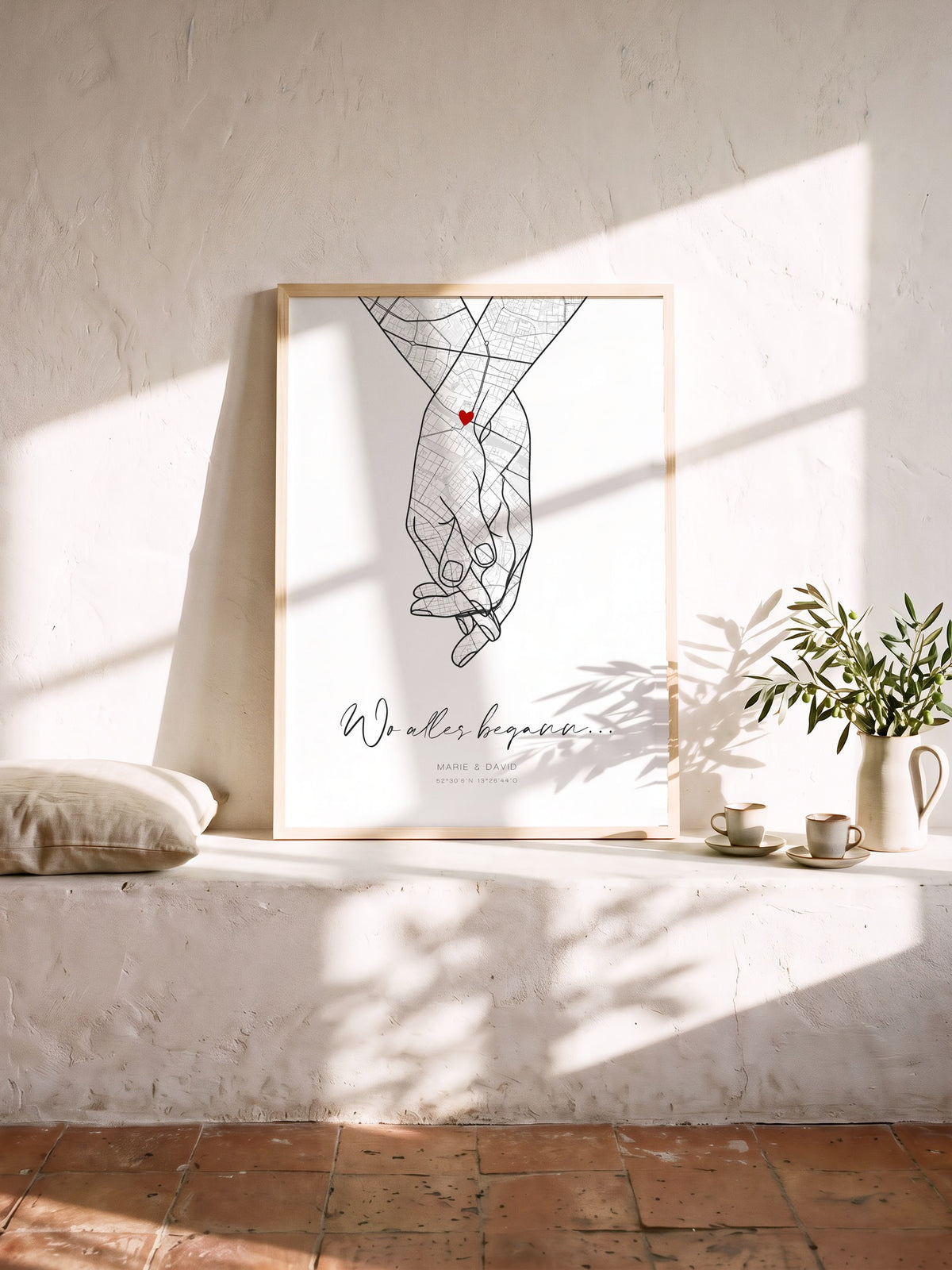 Hand-in-Hand-Kartenposter im Naturholzrahmen in einer sonnigen Kalkputznische, daneben Olivenzweig und zwei Tassen