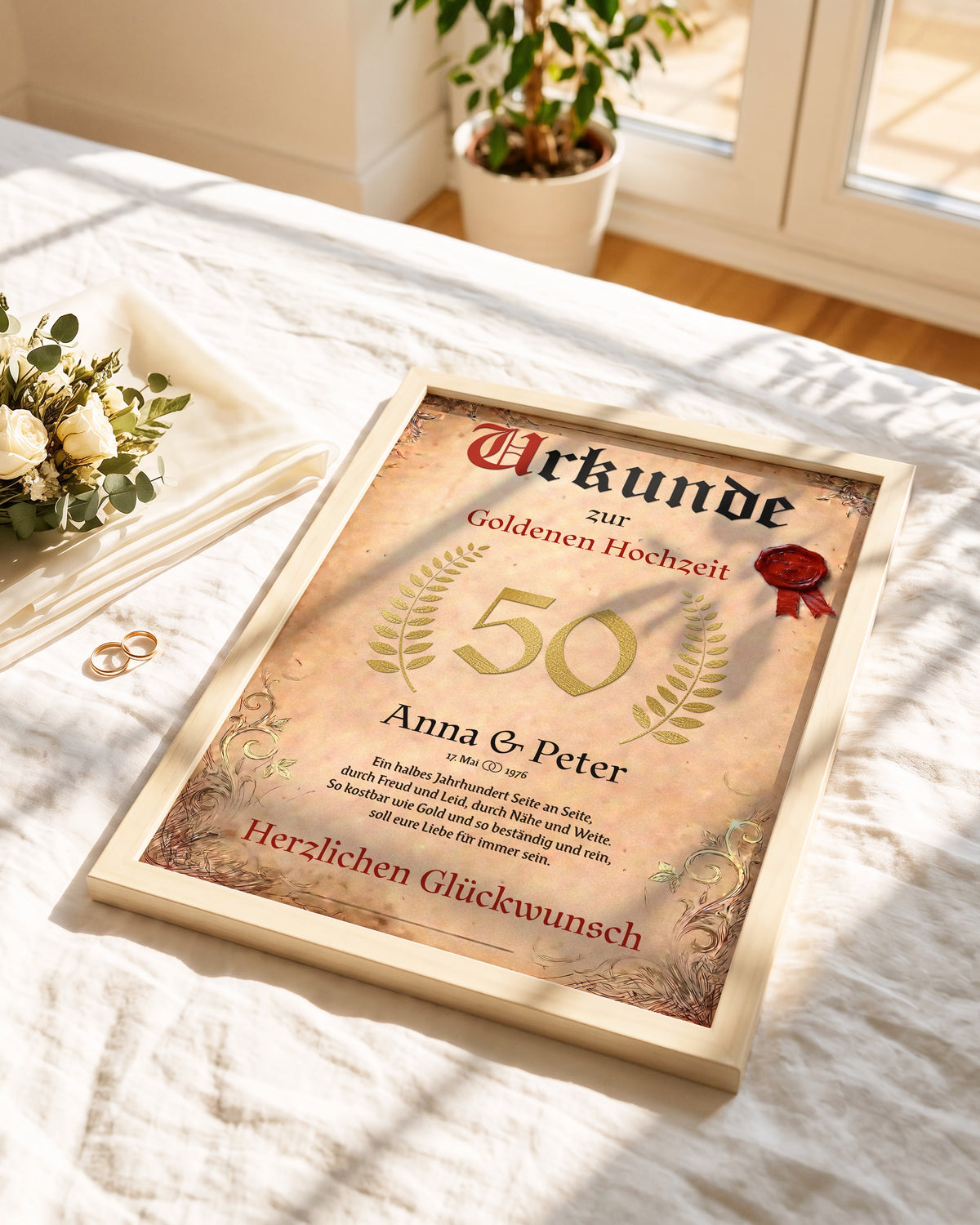 Urkunde zur Goldenen Hochzeit mit den Namen Anna und Peter im hellen Holzrahmen auf einem Leinenbett, daneben Eheringe