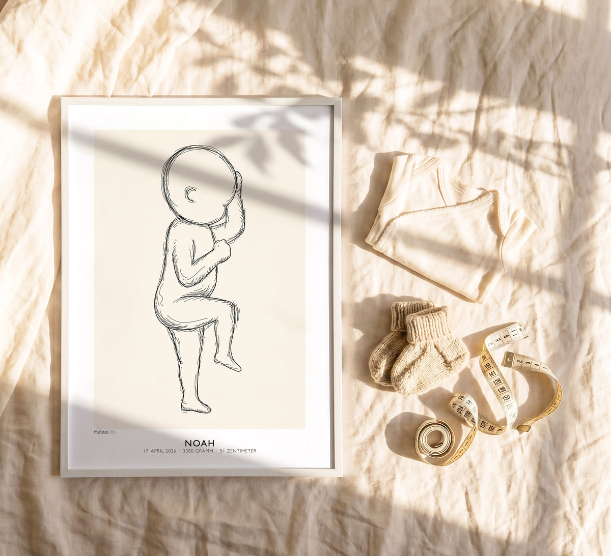 Geburtsposter von Noah in 50 × 70 cm im weißen Holzrahmen auf einem Bett neben Babybody, Söckchen und Maßband