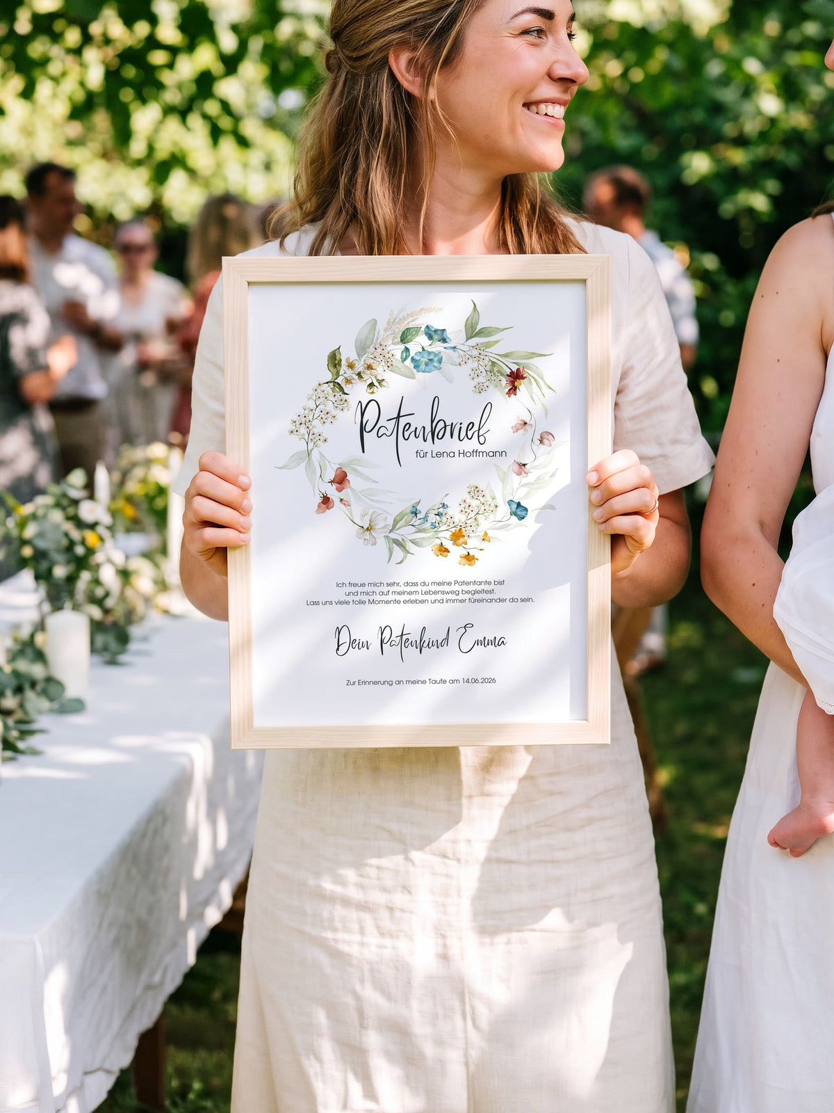Patentante hält den gerahmten Patenbrief beim Tauffest im Garten, neben ihr die Mutter mit dem Täufling