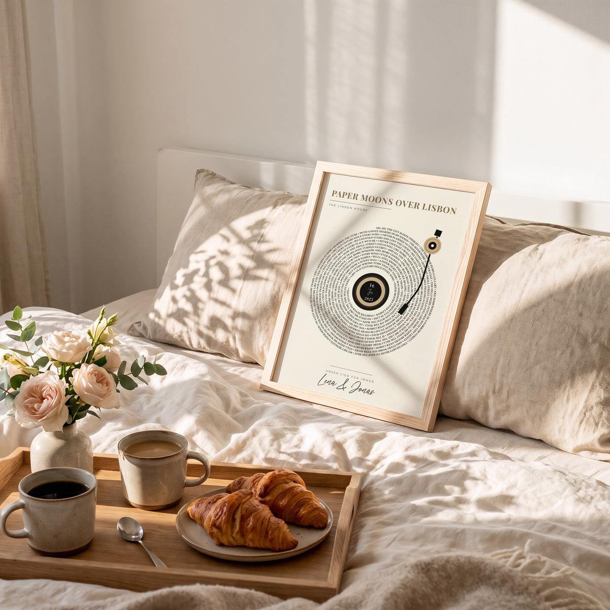 Songtext-Poster als Schallplatte in Sand im Holzrahmen auf dem Bett, davor Frühstück mit Kaffee und Croissants