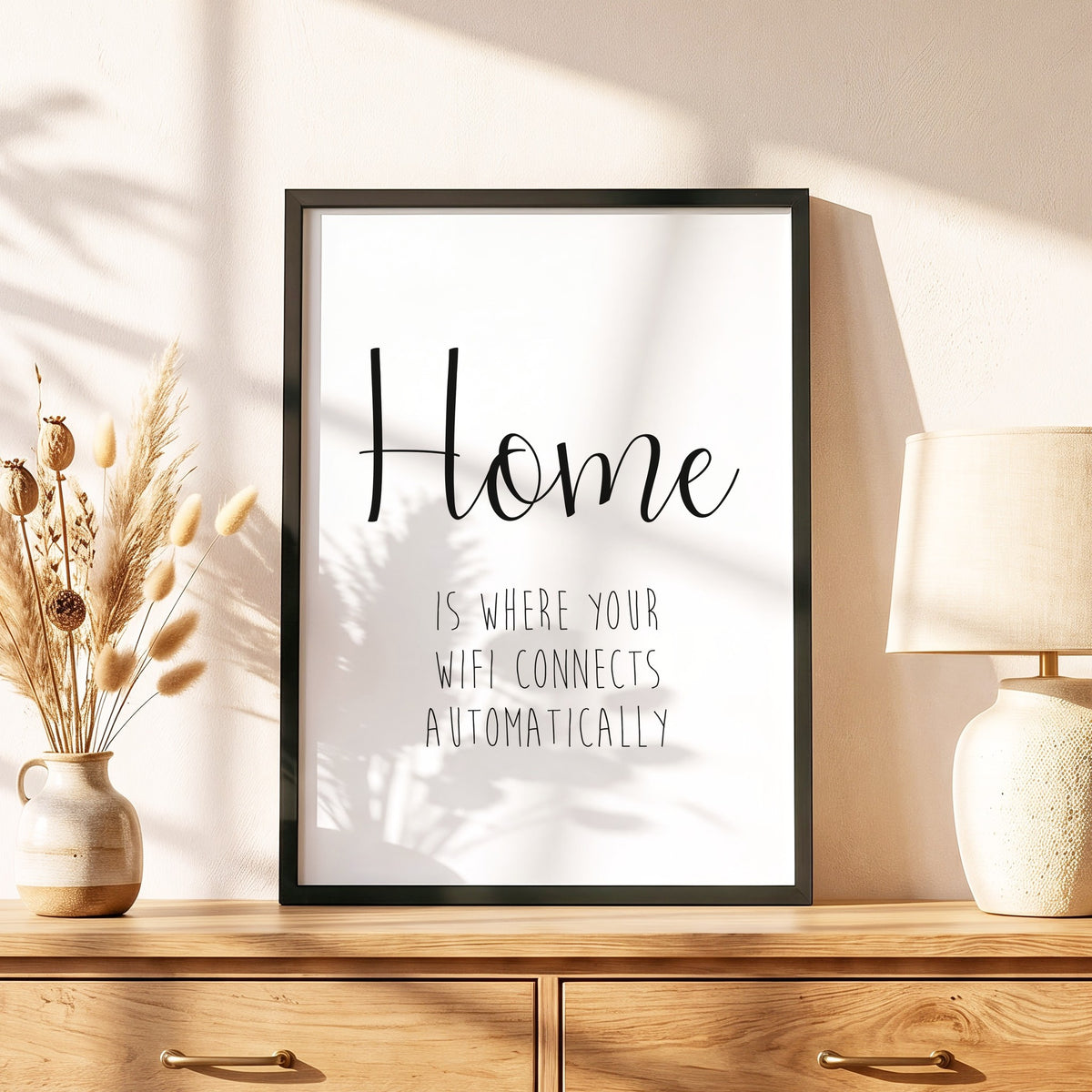 Spruchposter Home is where your wifi connects im schwarzen Holzrahmen auf einer Kommode