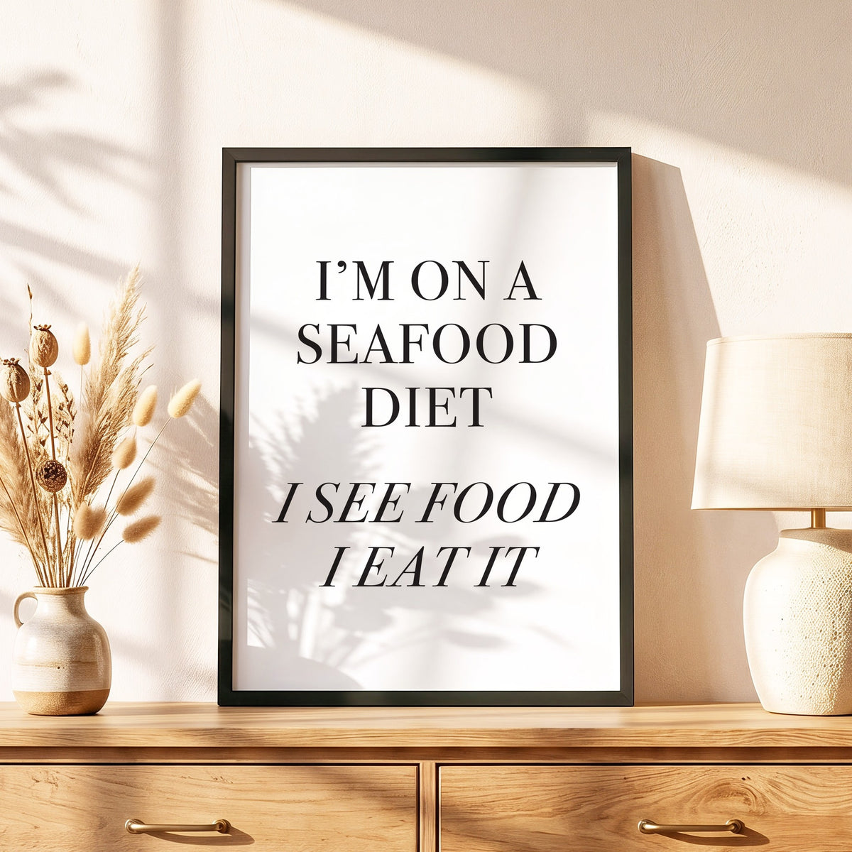 Spruchposter I'm on a seafood diet im schwarzen Holzrahmen auf einer Kommode
