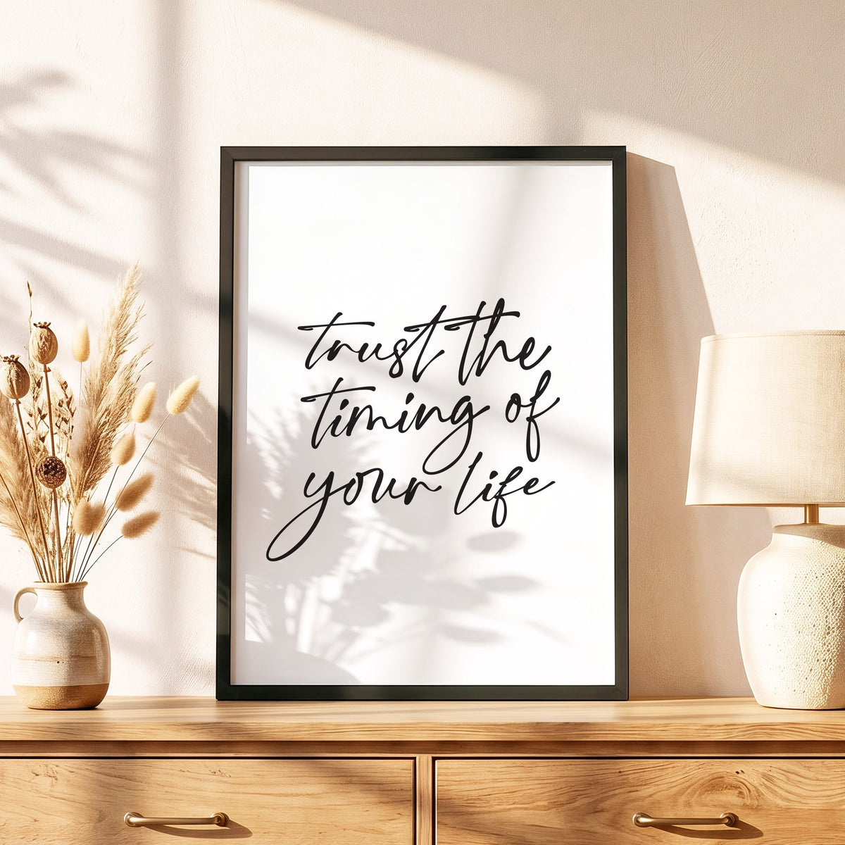 Spruchposter Trust the timing of your life im schwarzen Holzrahmen auf einer Kommode