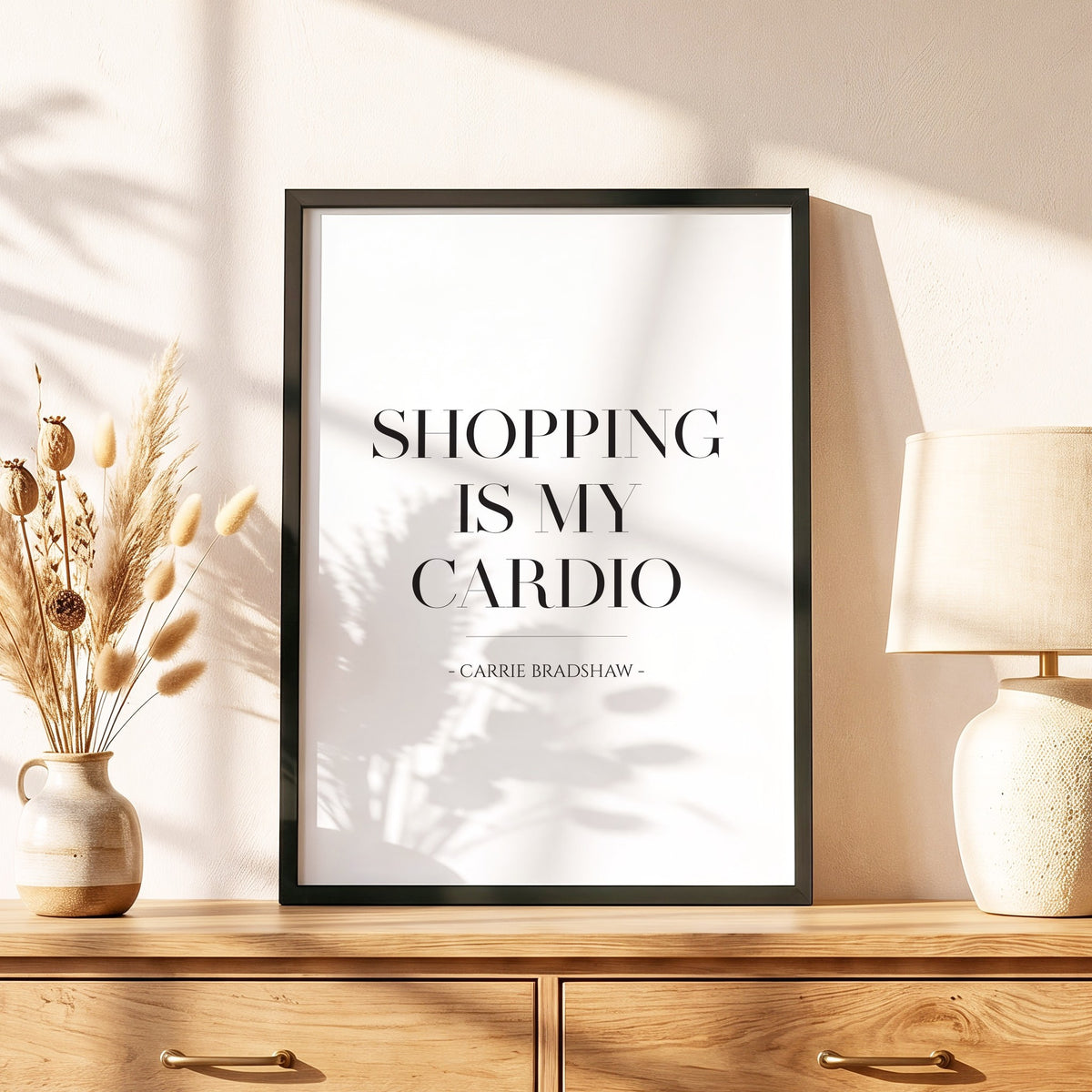 Spruchposter Shopping is my cardio im schwarzen Holzrahmen auf einer Kommode