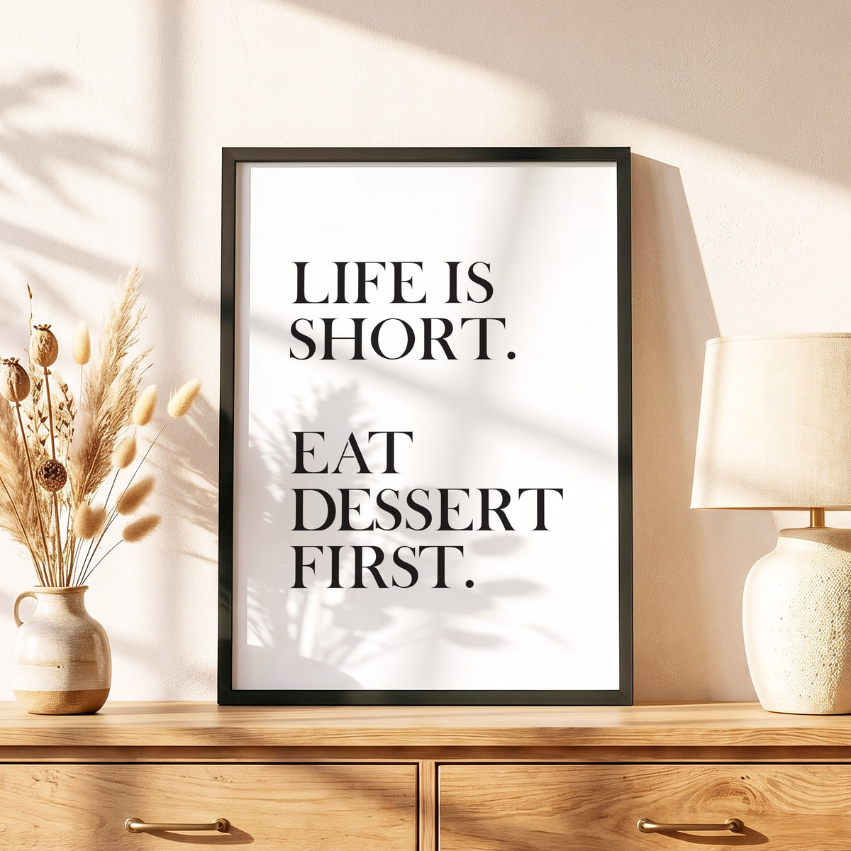 Spruchposter Life is short, eat dessert first im schwarzen Holzrahmen auf einer Kommode