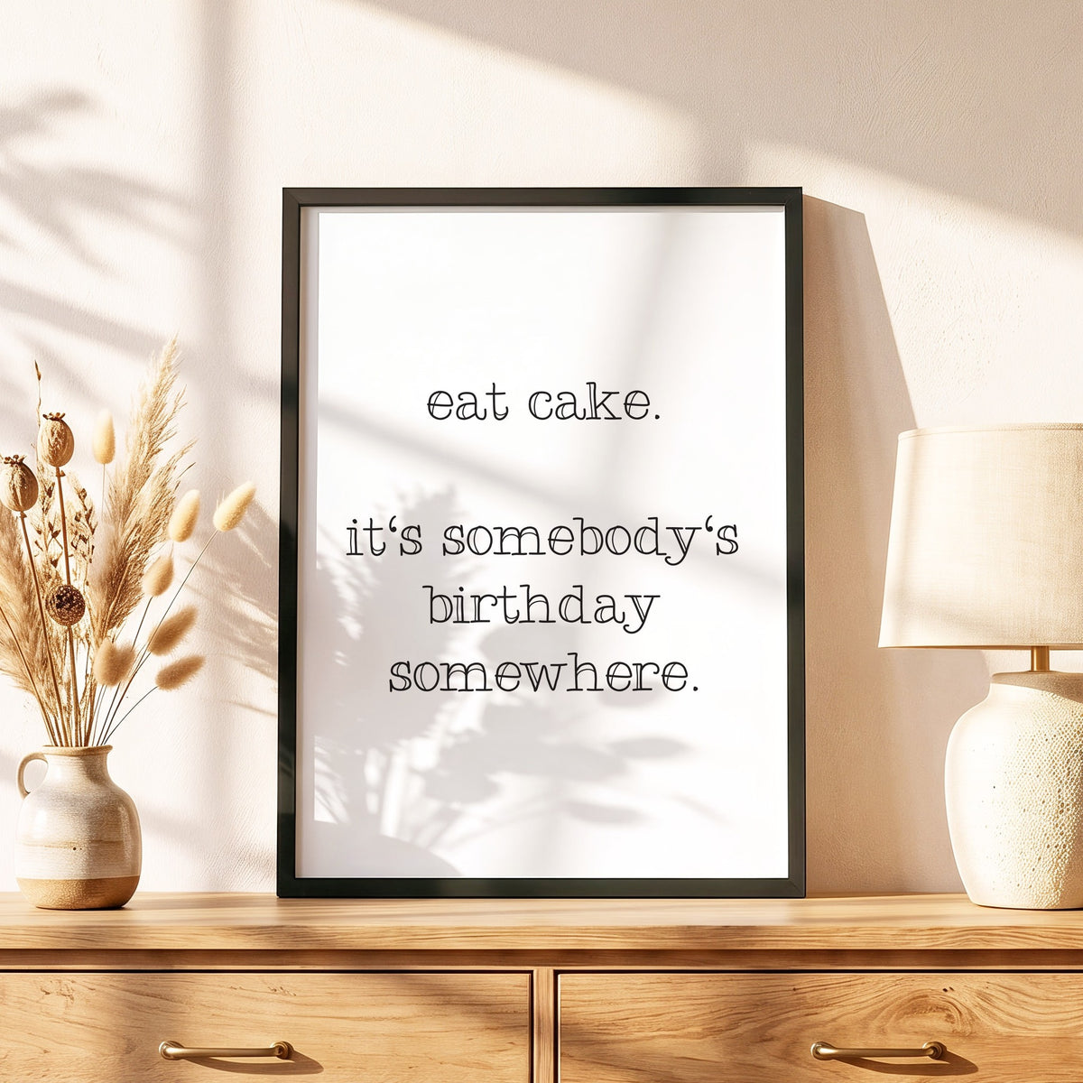 Spruchposter Eat cake im schwarzen Holzrahmen auf einer Kommode