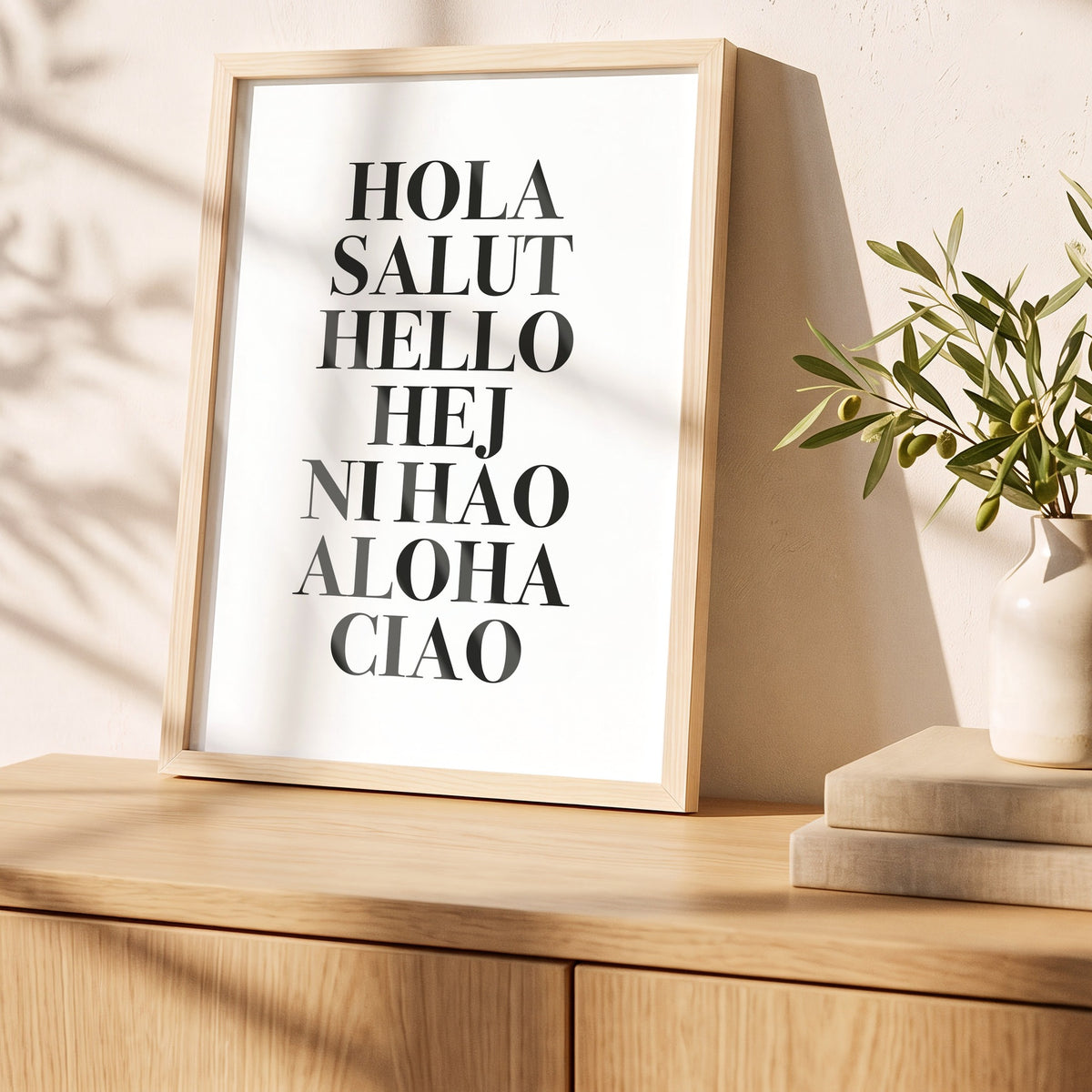 Poster Hola Salut Hello Ciao im Holzrahmen auf einem Sideboard