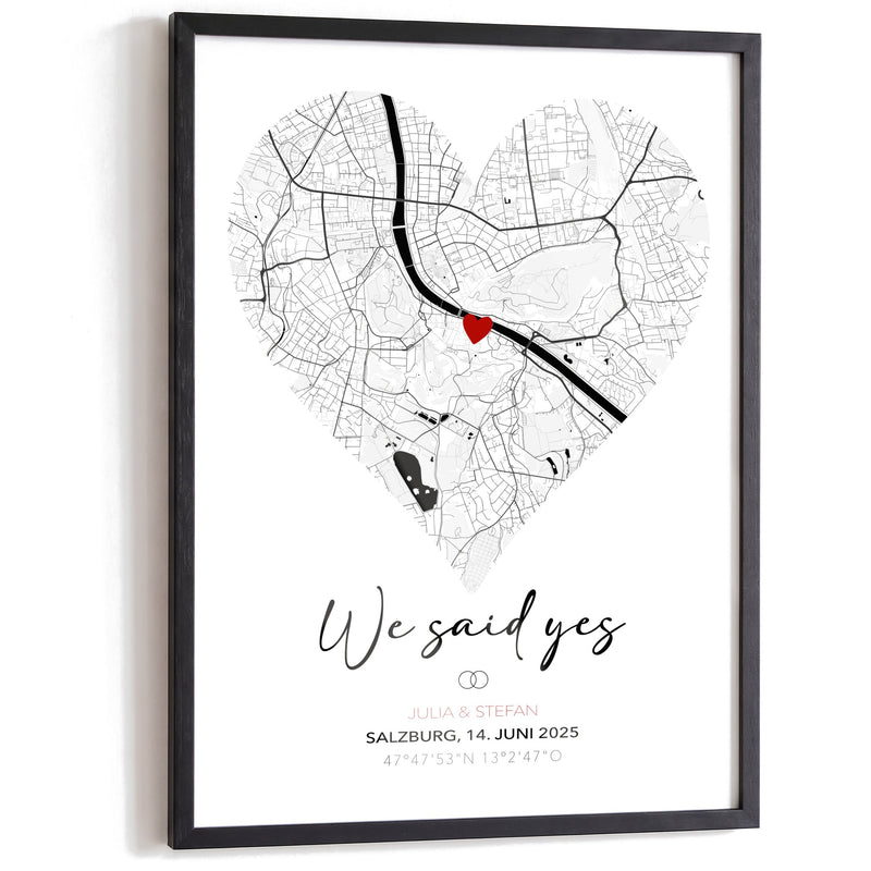 We-said-yes-Poster: Stadtkarte von Salzburg als Herz mit rotem Herz am Ort, Titel We said yes, Ringe, Namen, Ort, Datum und Koordinaten, im schwarzen Holzrahmen auf Weiß